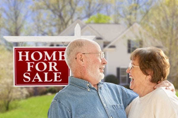 Senior Couple Front of For Sale Real Estate Sign and House